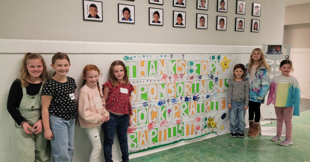 Welcome banner with kids from the church and pictures of students from the sponsor class