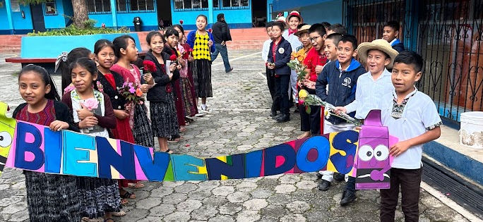 Guatemalan children in traditional dress holding a handmade banner that says Bienvenidos