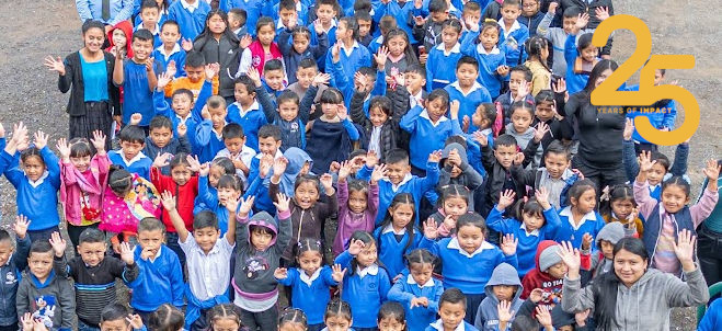 A crowd of children and teachers looking up and waving. 25 Years of Impact Logo in top right corner