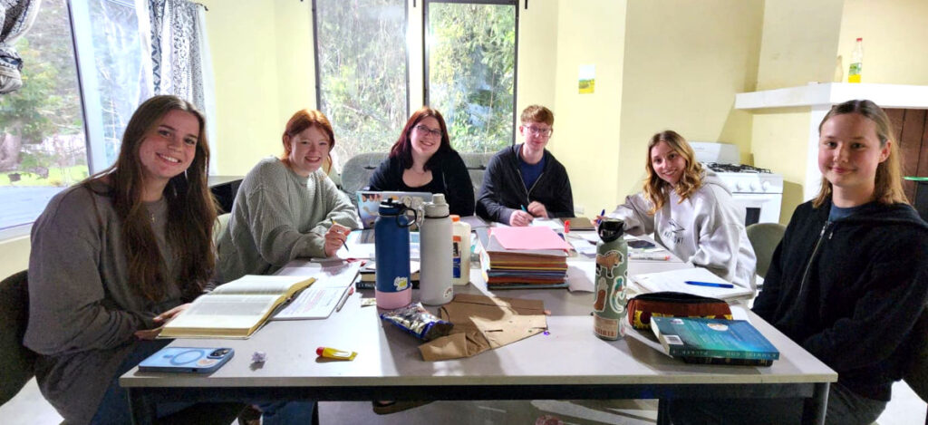 six young adults sitting around a table with notebooks open in front of them