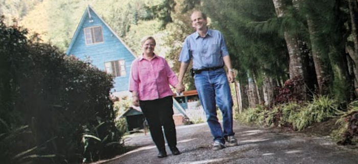 A young Rita and Les holding hands with a blue A-frame house in the background