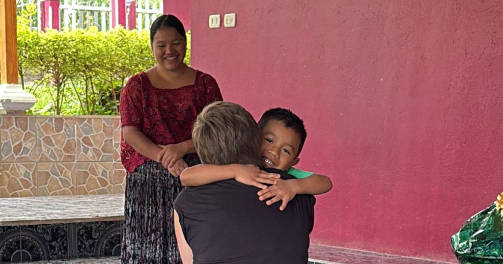 sponsor hugging child while mother smiles in background